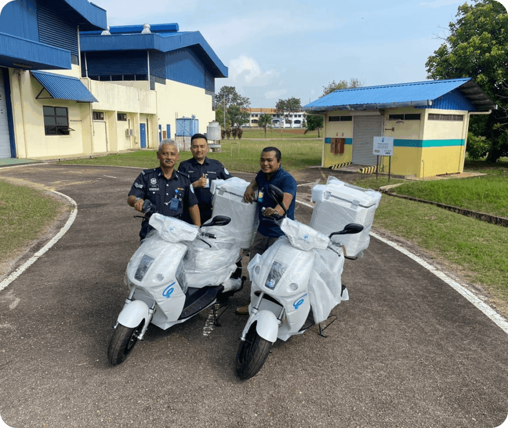 Three men in dark uniforms stand beside three white scooters wrapped in plastic, outside industrial buildings